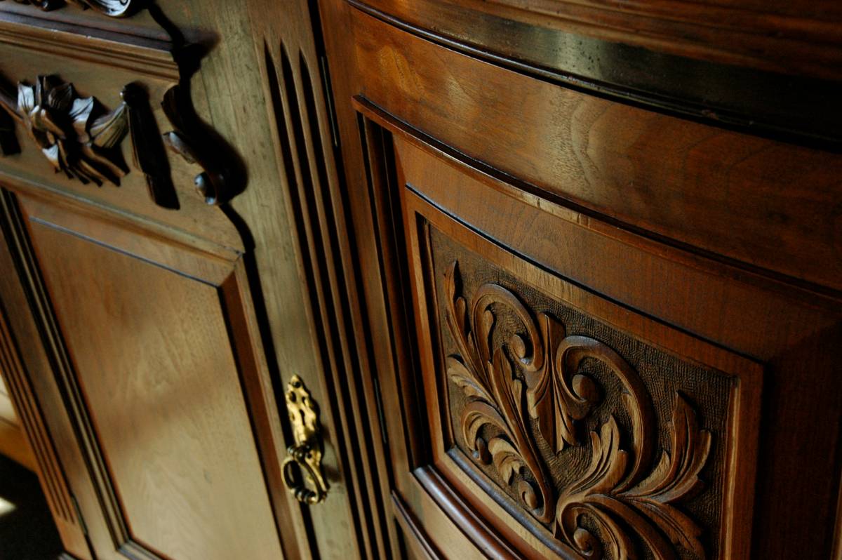 antique estate cupboard with hand-carved panels and brass hardware in dim auction hall lighting